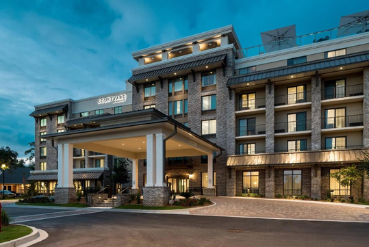 Four-story hotel building with a well-lit entrance, labeled "Courtyard," featuring large windows and a covered driveway.