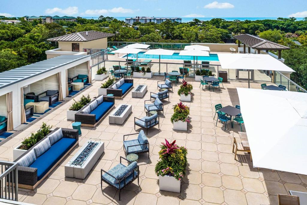 Rooftop terrace with seating areas, cabanas, planters, and a swimming pool, surrounded by greenery and under a clear sky.