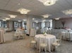 A banquet hall set up with round tables covered in white tablecloths and white chairs. Buffet tables are arranged along the walls.