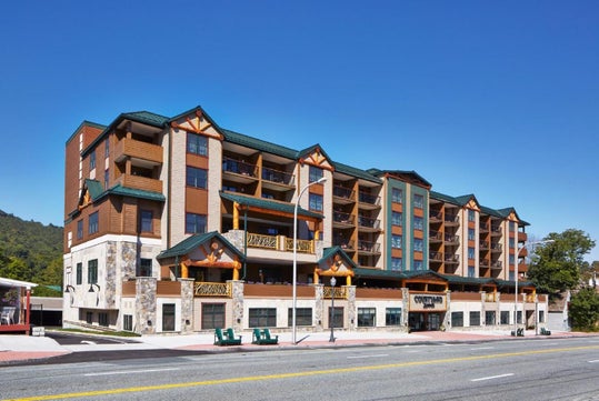 A five-story hotel building with wood accents and balconies under a clear blue sky, surrounded by mountains.