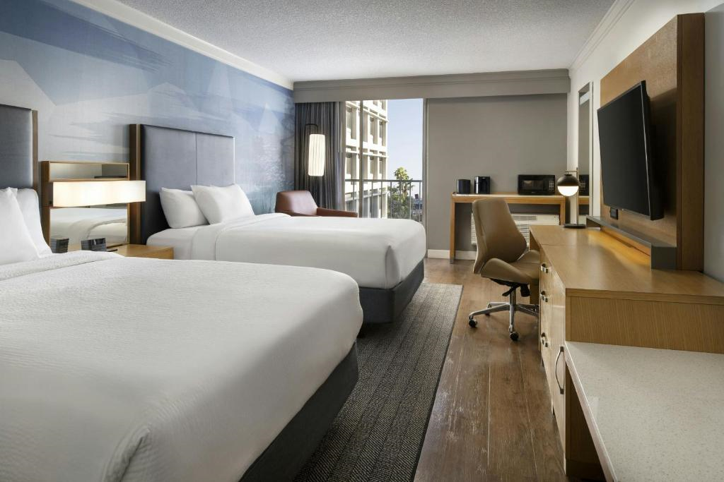 Guest room with 2 double beds, armchair, desk, office chair, and a wall-mounted TV.