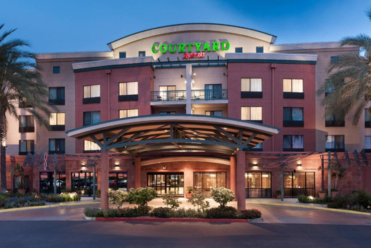 Front view of a Courtyard by Marriott hotel with a covered entrance, surrounded by palm trees and landscaping.