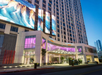 Tall modern hotel building with Courtyard and Residence Inn signage, large digital screens, glass entrance, and trees on the street at dusk.