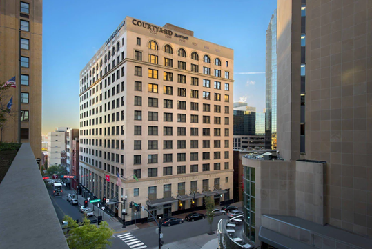 A multi-story Courtyard by Marriott hotel stands at a city intersection, surrounded by other tall office buildings and busy streets.