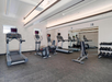 A gym room with treadmills, elliptical machines, a stationary bike, a set of dumbbells on a rack, and a large wall mirror.