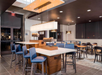 Modern dining area with high-top tables, blue upholstered chairs, pendant lighting, and a mix of seating arrangements on a tile floor.