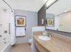 Modern bathroom with a granite countertop, a sink, a bathtub-shower combo, a toilet, white towels, framed art, and toiletries. Walls are light grey with an accent wall.