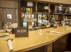Empty bar counter with wine glasses, napkins, and a menu labeled "The Bistro." Background features taps, liquor bottles, and menu boards.