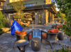Outdoor patio area with wicker chairs and orange cushions around a small pool. A blue covered object is nearby, and a building with a stone exterior is in the background.