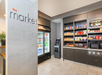 A small market setup with a fridge containing beverages, shelves stocked with snacks, and a microwave. An ATM is positioned next to the snack shelves.