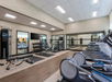 A modern gym with treadmills, stationary bikes, weight benches, a set of dumbbells, and large wall mirrors. Brightly lit with overhead lights.