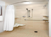 Accessible shower with a handheld showerhead, grab bars, wall-mounted foldable seat, and a white curtain in a tiled bathroom.