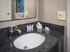 A bathroom sink with a granite countertop features a modern faucet, toiletries, rolled towels, and a wall-mounted electrical outlet beside a mirror.