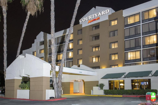 Exterior view of a Courtyard by Marriott hotel at night, with illuminated windows, palm trees, and a covered entrance.