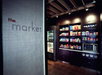 A small self-serve market with shelves of snacks, a microwave, drink coolers, and a coffee machine; "the market" sign on the wall.
