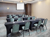 Meeting facility with long tables, chairs and a white projector screen.