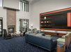 Modern lounge with a large sectional sofa, armchairs, a fireplace, and a wall-mounted TV. Decor includes shelves with vases and art pieces. Large windows provide natural light.