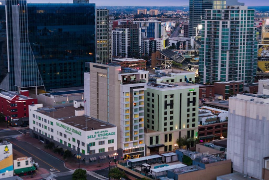Skyline view of a city with modern high-rise buildings, including a self-storage facility in the foreground, at dusk.