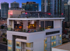 Rooftop view of a modern building with outdoor seating area amidst a cityscape at dusk, surrounded by tall skyscrapers.