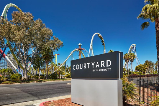 Sign for Courtyard by Marriott with roller coasters in the background under a clear blue sky.