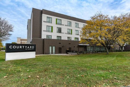 Four-story Courtyard by Marriott hotel with green and white accents, located next to a grassy area with trees.