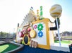 Colorful, whimsical building with gear shapes, pipes, and candy-like decorations, resembling a playful factory or funhouse at an outdoor mini-golf course.