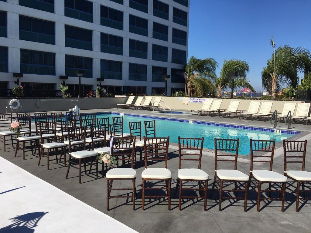 Outdoor venue with rows of chairs facing a pool, set up for an event. A high-rise building is in the background, with palm trees around the area.