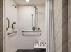 Accessible walk-in shower with a wall-mounted showerhead, adjustable handheld shower, grab bars, fold-down bench, soap dispensers, and a curtain.