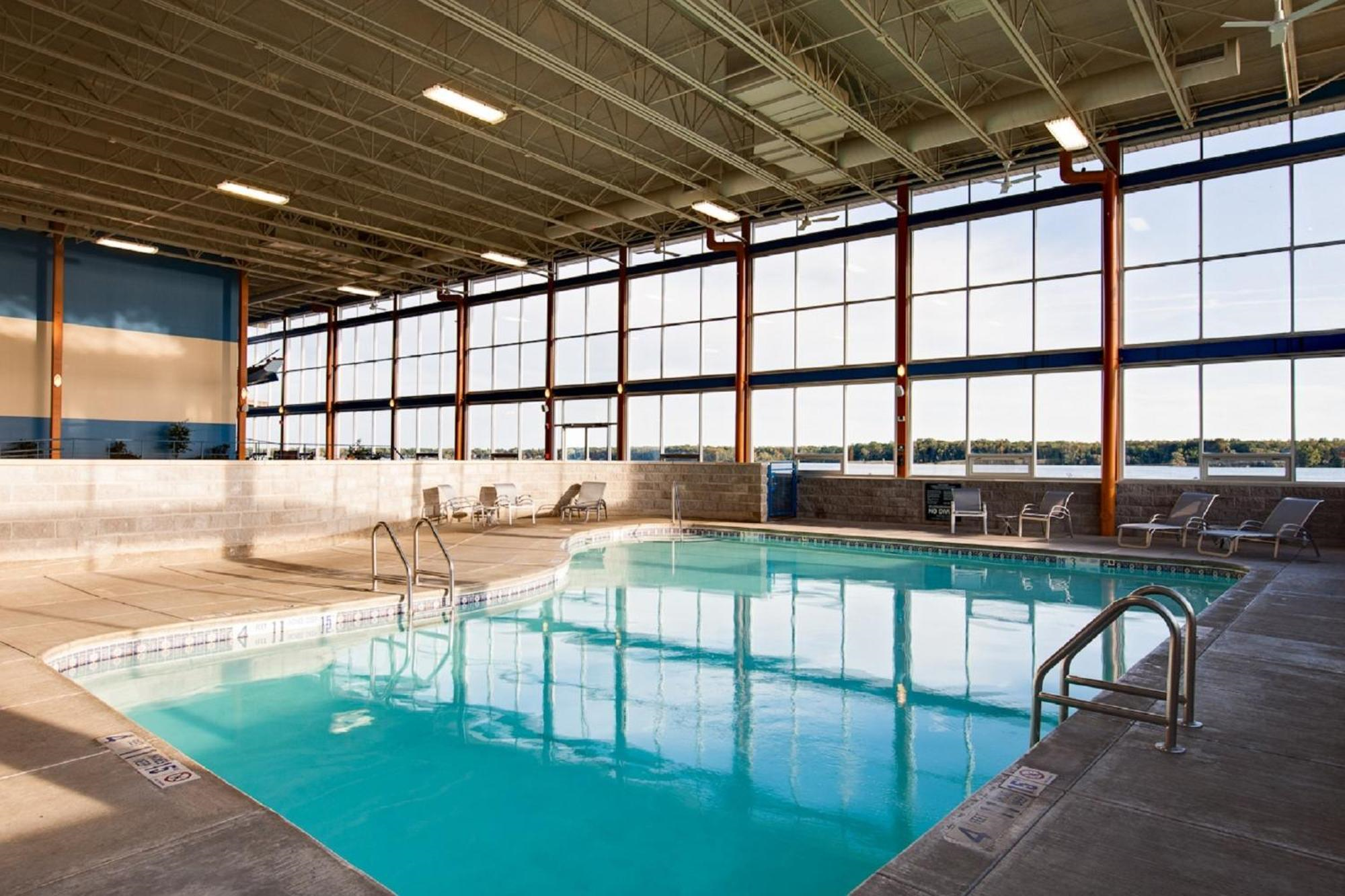 Indoor swimming pool with clear water, surrounded by lounge chairs, large windows, and high ceiling allowing natural light in.