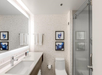 Modern bathroom with a sleek vanity, large mirror, and glass shower. Two framed artworks and white towels hang on the wall.