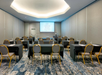 A conference room with rows of tables and chairs facing a projector screen displaying "Crowne Plaza.