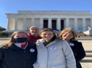 Four people stand smiling in front of the Lincoln Memorial. One is wearing a face mask. All have "I Voted" stickers on their jackets.