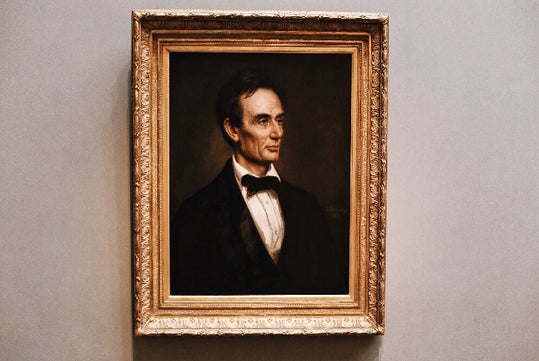 A framed portrait of a man in formal attire, shown from the chest up, set against a plain background.