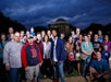 A large group of people poses together outdoors at dusk, with the Jefferson Memorial visible in the background.