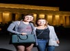 Two women stand together and smile for a photo at night in front of the illuminated Lincoln Memorial.