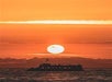 Sunset cruise boat sailing under a glowing orange sky in Newport Beach.