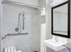 Accessible bathroom with a shower bench, handheld showerhead, grab bars, mirror, and sink.