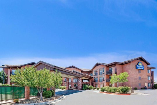 Two-story brick hotel with brown roof, featuring a covered entrance and "Days Inn" signage. Surrounded by small trees and bushes under a clear blue sky.