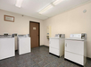 Laundry room with four white machines—two washers and two dryers—on a tiled floor, with a vending machine and a closed door in the background.