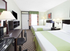 Two queen beds, a work desk and a flat-screen TV inside a guest room.