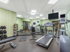 A gym room with treadmills, exercise bikes, weights on racks, yoga mats, and a wall-mounted TV.