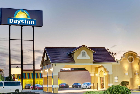 Days Inn hotel exterior at dusk with illuminated signage and multiple parked cars, featuring a tiled roof and archway entrance.