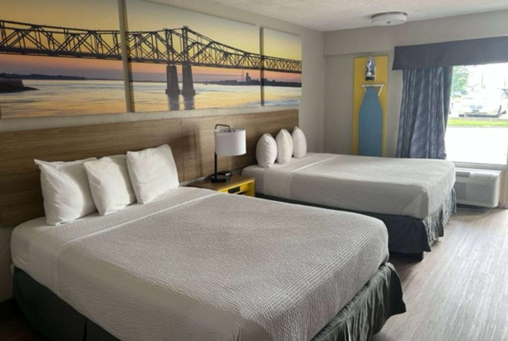 Hotel room with two double beds, white bedding, a nightstand with a lamp, large bridge photo above beds, gray curtains, and air conditioning unit by the window.