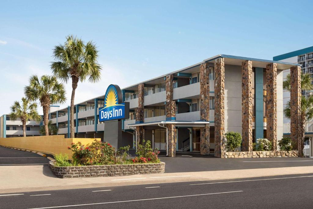 Exterior view of a Days Inn hotel featuring three stories, a stone facade, palm trees, landscaped plants, and a visible entrance with a parking lot in front.