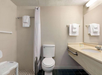 Accessible bathroom with a walk-in shower, shower chair, toilet, sink with grab bar, towel racks, and toiletries on the counter.