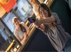A young woman aims a handgun and smiles at an indoor shooting range, while two people watch in the background.