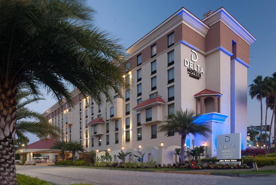 Exterior view of Delta Hotels building with palm trees and a well-lit entrance, set against a twilight sky.