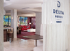 Hotel lobby with red and white decor, marble flooring, seating areas, and large windows. "Delta Hotels" sign visible on a partition.