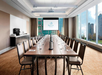 A conference room with a long table, chairs, a projector screen displaying "Delta Toronto," large windows, and a coffee station at the side.