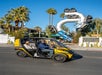 A man and woman driving a yellow GoCar on a sunny day on the Deluxe 2-Hour GoCar Las Vegas Strip Tour.